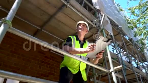 在建筑工地工作的男建筑工头工人或建筑师穿着安全帽站在脚手架上视频的预览图