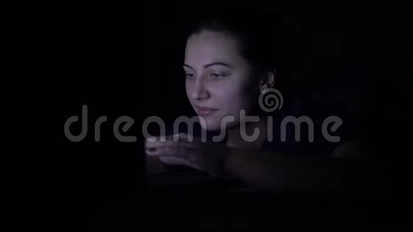 一个女人晚上躺在家里的床上用移动电脑在网上购买孤立光视频的预览图