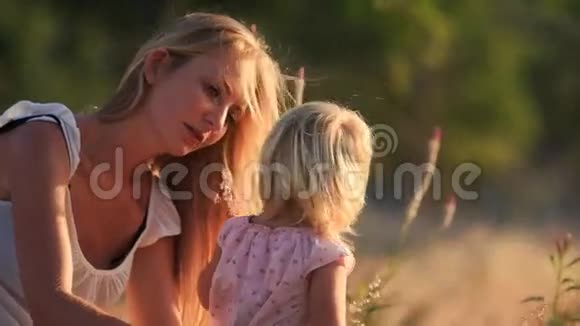 金发母亲给小女儿看草地上的田野花视频的预览图