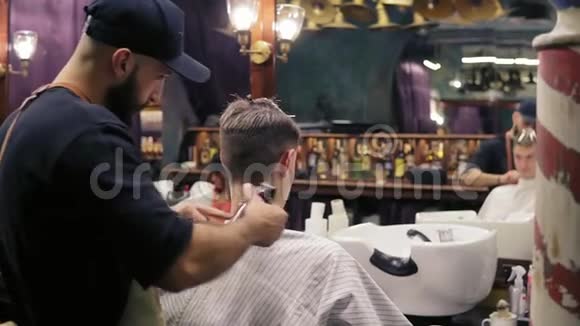 在理发店里一个留胡子的理发师用电动修剪器在他的顾客的脖子上剪头发慢动作视频的预览图