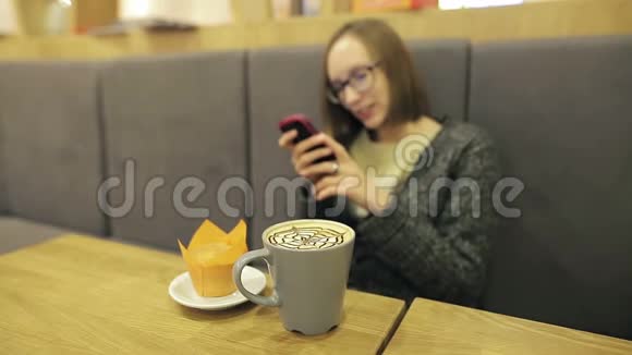 戴眼镜的孤独女孩在等她的男朋友她用智能手机在咖啡馆里喝椰子视频的预览图