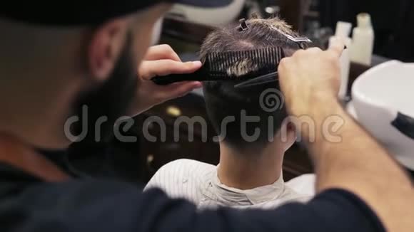 一位坐在镜子旁的客户的后景当时一位留胡子的理发师正在用剪刀剪头发他正在梳头视频的预览图