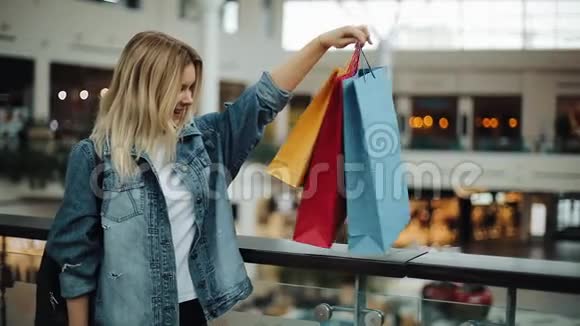 快乐的金发女孩看着站在购物中心的五颜六色的购物袋视频的预览图