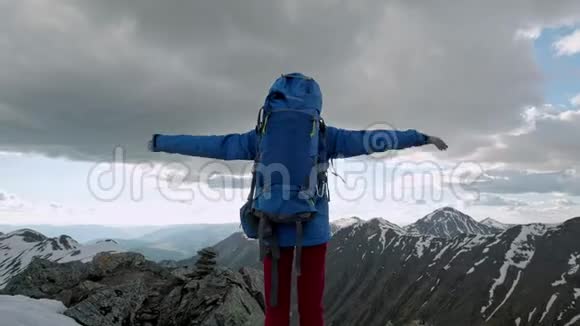 年轻快乐的女人背着背包站在岩石上举起双手望着下面的山谷视频的预览图