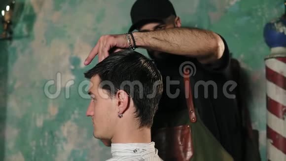一位发型师轻轻梳理了男性客户的短湿头发一位坐着一个男客户的头发梳着围裙的胡子理发师视频的预览图