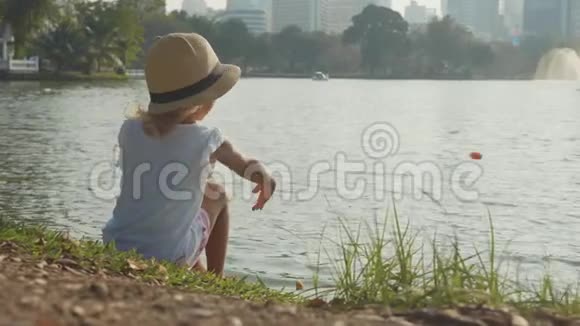 穿着乡村风格帽子的小女孩在公园湖里慢动作喂鱼视频的预览图