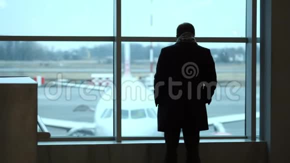 老人站在全高的位置凝视机场候机楼的窗外侧影观景在机场看飞机视频的预览图