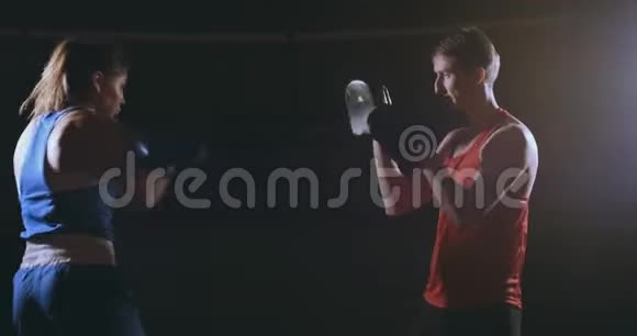 一个漂亮的黑发拳击手在黑暗的房间里和一个教练一起打爪子视频的预览图