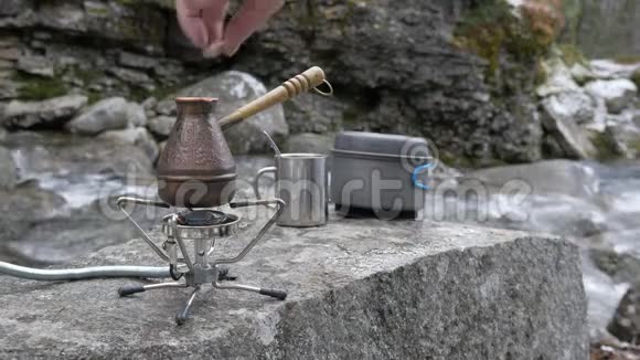 在便携式燃气燃烧器上有一个用来冲泡咖啡的水壶糖被扔进里面在河边野餐视频的预览图