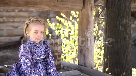 穿着传统服装的小漂亮女孩坐在一口古老的农村木井上的肖像双手交叉全高清视频的预览图