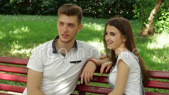 公园里一个漂亮的年轻女子和一个坐在长凳上的男人谈笑风生视频的预览图