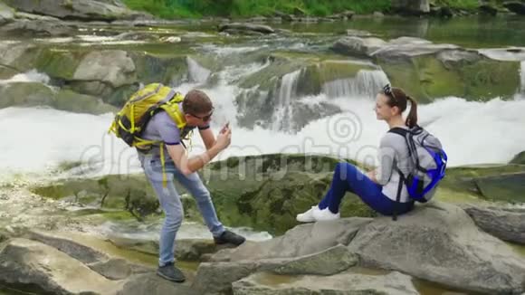 一个男人在一条河边风景如画的地方给他的女朋友拍照旅游和积极的生活方式视频的预览图