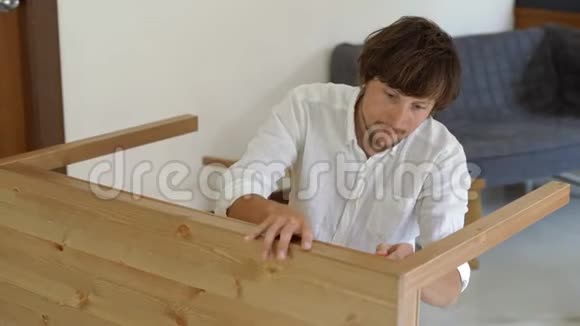 一位年轻男子的专业家具装配工在厨房里组装了一张木桌视频的预览图