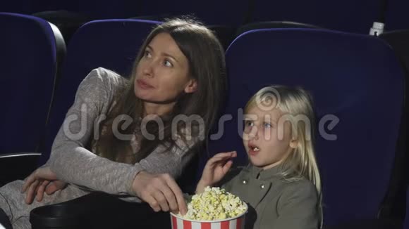 美丽的女人和她的小女儿在电影院吃爆米花看电影视频的预览图
