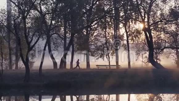 一个女人在秋天的雾天日出期间在公园里奔跑的剪影视频的预览图