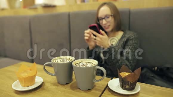戴眼镜的女人在咖啡馆里使用智能手机上的应用程序喝椰子咖啡微笑着在手机上发短信美丽美丽视频的预览图