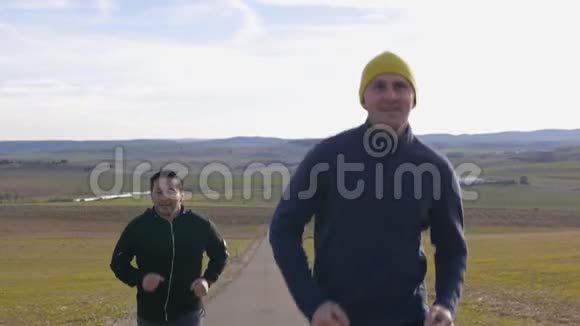 与户外私人教练一起健身两个男人在丘陵地带的乡间小路上慢悠悠地慢跑视频的预览图