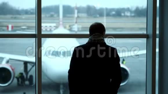 老人站在全高的位置凝视机场候机楼的窗外侧影观景在机场看飞机视频的预览图