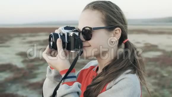 一个戴太阳镜的年轻女孩在老式相机上拍摄大自然的照片视频的预览图
