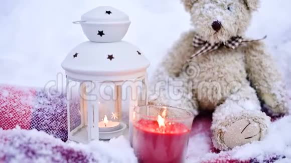 一只玩具熊的特写镜头在洒满雪堆的户外舒适的格子地毯上放上圣诞蜡烛视频的预览图