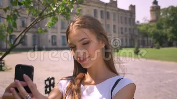 漂亮的年轻女人白天站在公园里在智能手机上自拍交流理念视频的预览图