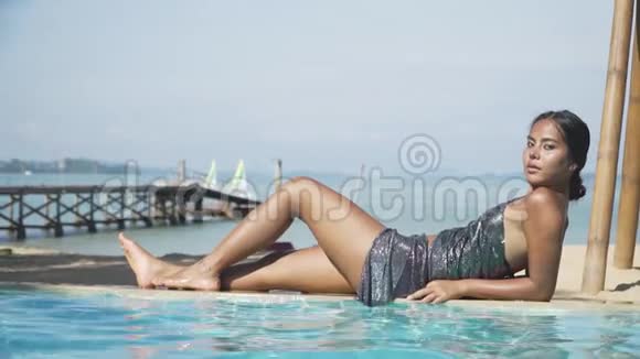 亚洲模特女孩躺在靠近水的池边一件闪亮的连衣裙上视频的预览图