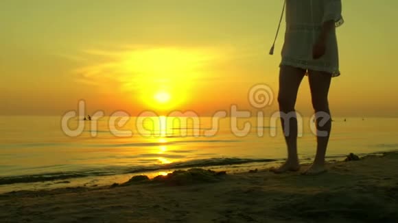 一个年轻的女人在夕阳的背景下赤脚走在沙滩上3这女孩走路很慢视频的预览图