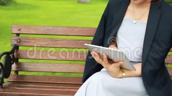 年轻漂亮的女人带着平板电脑坐在花园里视频的预览图