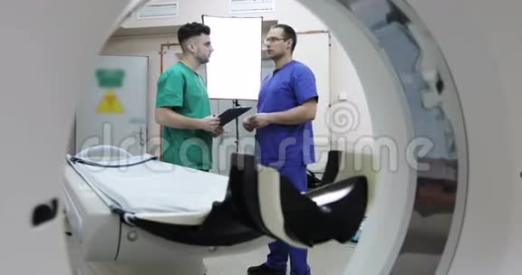 4两位年轻的医生用CT扫描仪在房间里讨论病人的治疗视频的预览图