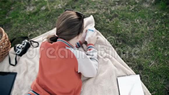 年轻的女人在公园里放松手机躺在绿色的春天草地上的地毯上视频的预览图