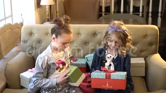 假日概念两个漂亮的小女孩坐在一起拿着明亮的盒子和礼物试图打开它们适用范围视频的预览图