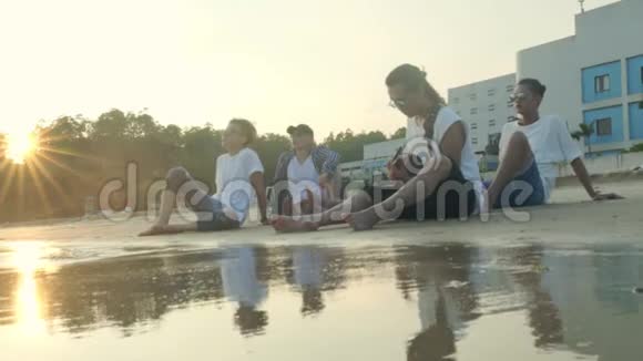 年轻的亚洲成年人坐在沙滩上放松地弹吉他视频的预览图