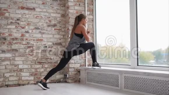 年轻女子靠在窗台上伸展腿部肌肉视频的预览图