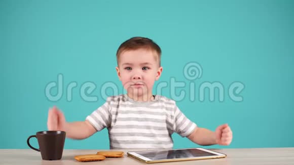 可爱的小男孩坐在桌子上玩平板电脑孩子在喝茶视频的预览图