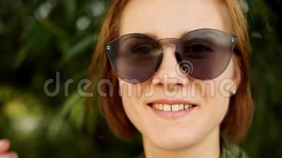 一位戴墨镜的红发女孩在夏日绿茵背景下的失色肖像自然美景夏日视频的预览图