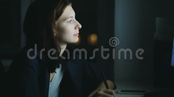 晚上在办公室工作的集中女性设计师使用电脑和图形平板电脑的特写手持镜头视频的预览图