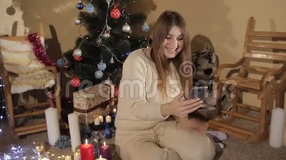 年轻漂亮的女孩坐在圣诞树旁除夕夜在Skype上聊天视频的预览图