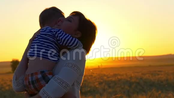 快乐的母亲抱着她的孩子在一片麦田的夕阳背景下幸福家庭的概念视频的预览图