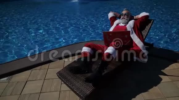 圣诞老人在游泳池日光浴有趣的是使用笔记本电脑视频的预览图