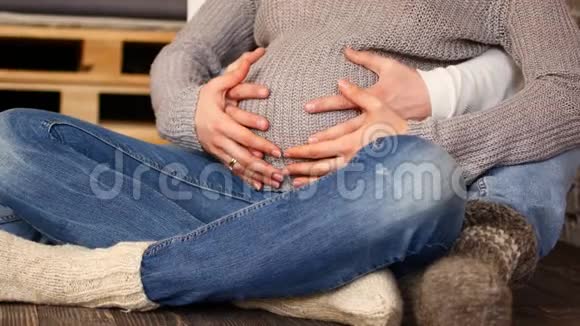 妈妈和爸爸手在怀孕的肚子上显示心脏的迹象怀孕夫妇抚摸怀孕的肚子准妈妈照顾视频的预览图