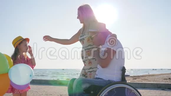 坐轮椅的残疾人有家人母亲小女孩在夏天在沙滩上听爸爸妈妈的话视频的预览图