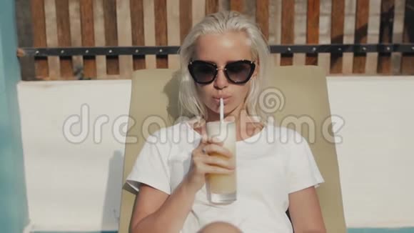 漂亮又合身的年轻女人留着长长的直发在海边的躺椅上放着一杯橙汁视频的预览图