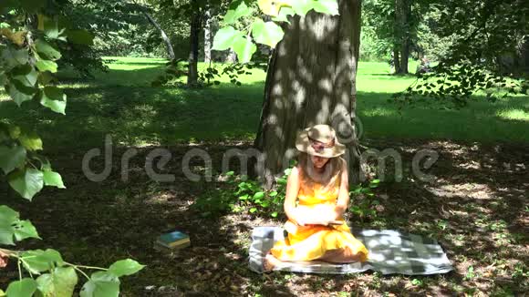女人坐在格子布上在树影下的公园里看书4K视频的预览图