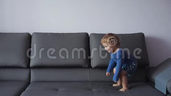 金发卷曲的小女孩跳上沙发蓝色的衣服感觉很开心慢动作视频的预览图
