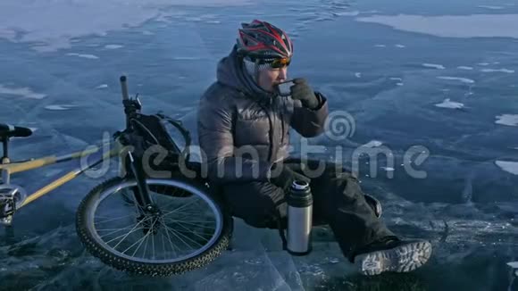 那个人正坐在冰上自行车的轮子上休息他喝热水瓶里的茶骑自行车的人穿着视频的预览图