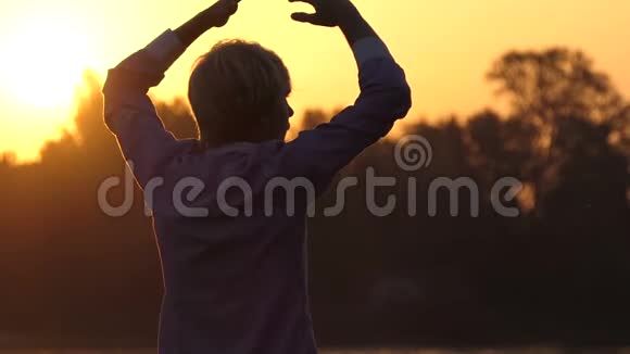 在太阳落山的时候金发男人在湖岸做瑜伽练习视频的预览图