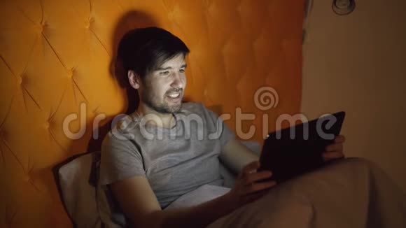 年轻开朗男子使用平板电脑与女友在线视频聊天前躺在床上视频的预览图