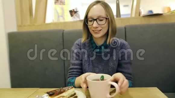 年轻漂亮的戴眼镜的女孩在咖啡馆喝了无味的茶后做了个鬼脸不满意的顾客感到震惊视频的预览图