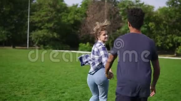 后景拍摄可爱迷人的国际情侣手牵着手在草地上奔跑视频的预览图