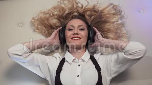 女人躺在床上戴着大耳机听音乐对她性感微笑的中间框架有反应视频的预览图